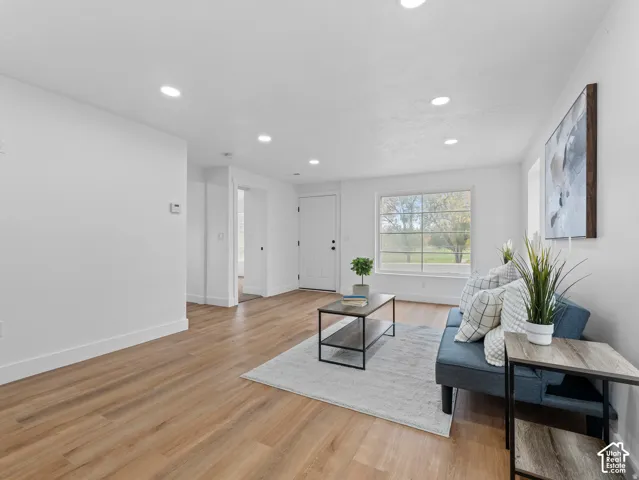 Recessed ceiling lighting illuminates a spacious living area featuring wood-finish flooring and white walls