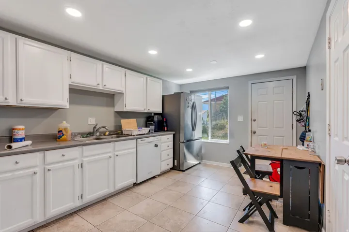 Kitchen featuring white cabinetry, light countertops, stainless steel refrigerator, white dishwasher, and tiled flooring