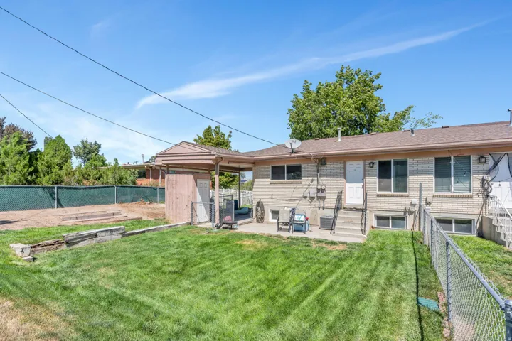 Expansive rear yard with a manicured lawn, brick exterior, covered patio area, and concrete stairs with metal railings