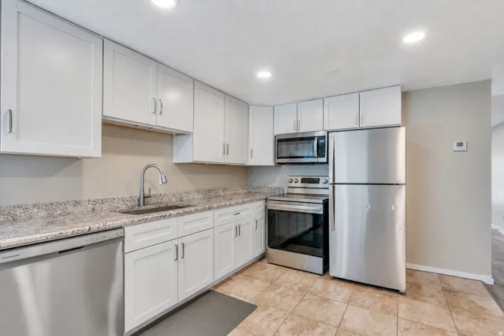 White cabinetry with brushed nickel hardware, speckled countertops, stainless steel appliances, and tile flooring
