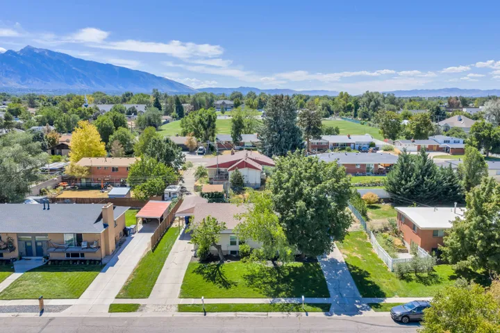 Aerial property view featuring a manicured lawn, established trees, and a mountain backdrop