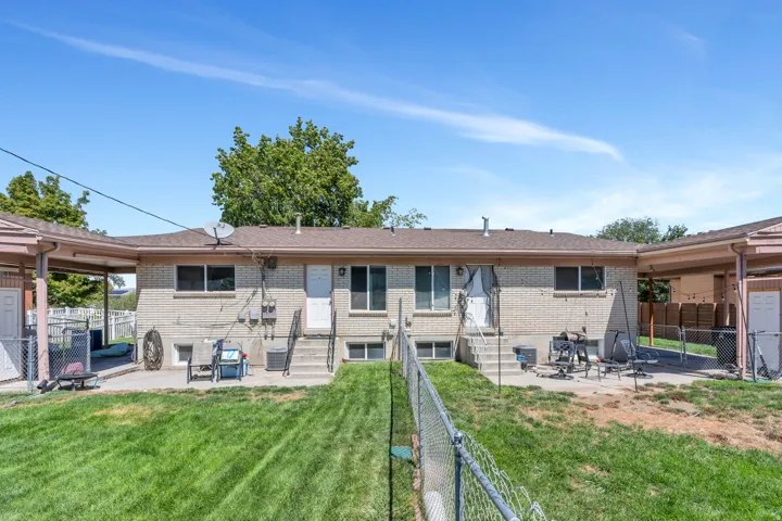 Expansive backyard featuring a manicured lawn, chain link fencing, a concrete patio, and a covered carport structure