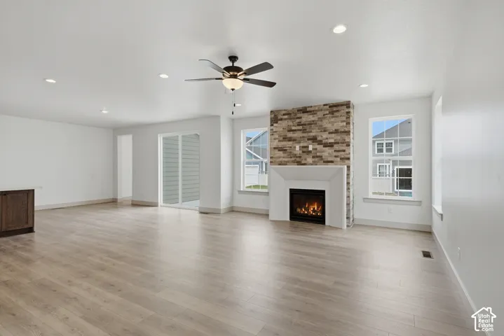 Spacious living area featuring wood-finish flooring, a contemporary fireplace with a stone surround, recessed lighting, and a ceiling fan