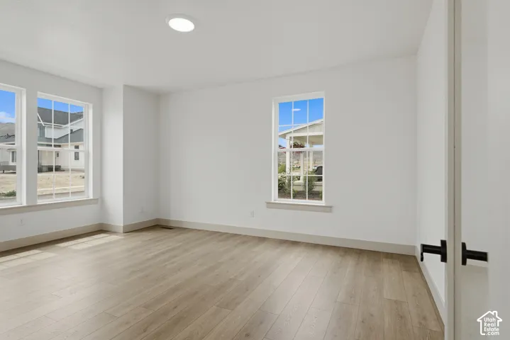 Recessed ceiling lighting illuminates a room featuring wood-finish flooring, multiple windows, and white walls, complemented by a white bifold door with black hardware