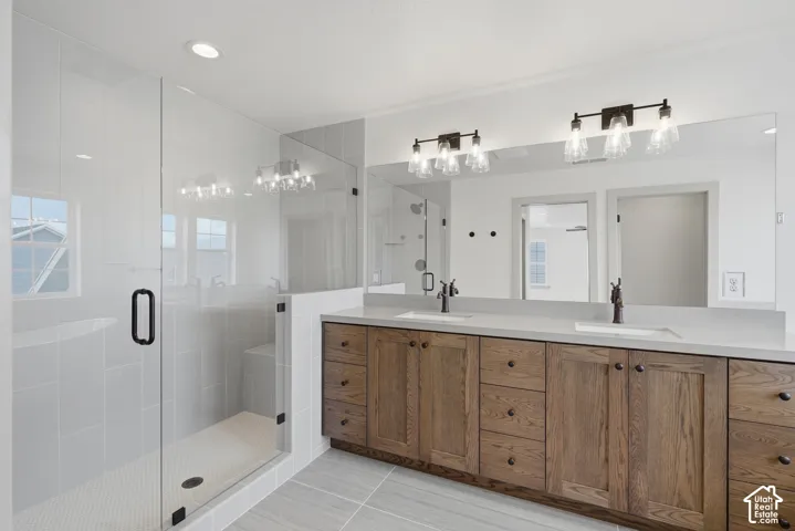 Primary Suite. Spacious bathroom featuring a frameless glass shower enclosure, dual vanity with wood-finish cabinetry, white countertop, and contemporary lighting fixtures