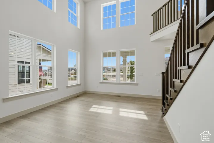 Two-story entry with multiple windows, wood-finish flooring, and a dark wood and white spindle staircase
