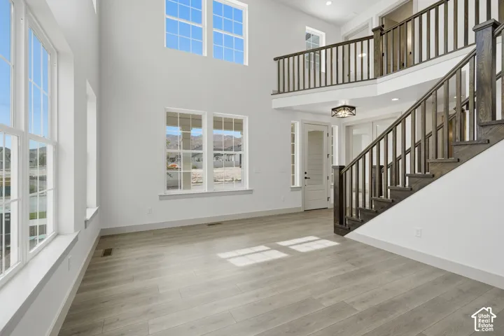Vaulted ceiling with high windows, light wood-finish flooring, dark wood staircase, and an upper-level balcony with matching dark wood railing