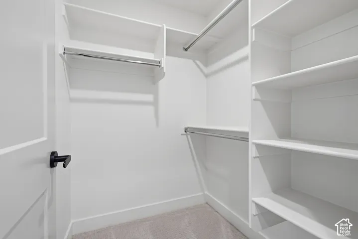 Primary Suite, closet 2. White built-in shelving, chrome hanging rods, paneled door with matte black hardware, and gray carpeting