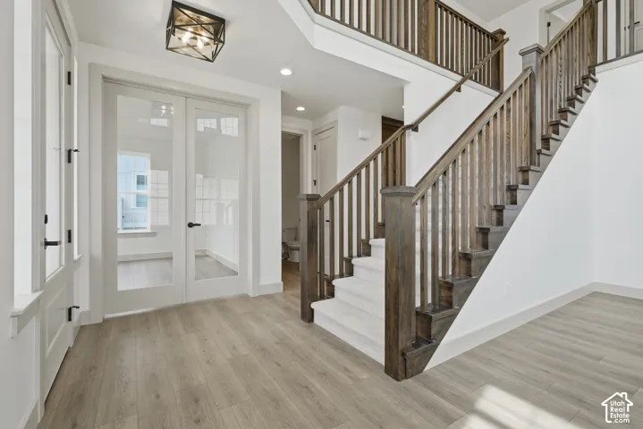 Wood-finish flooring, two-story staircase with dark wood newel posts and railings, carpeted stairs, and a decorative ceiling light fixture