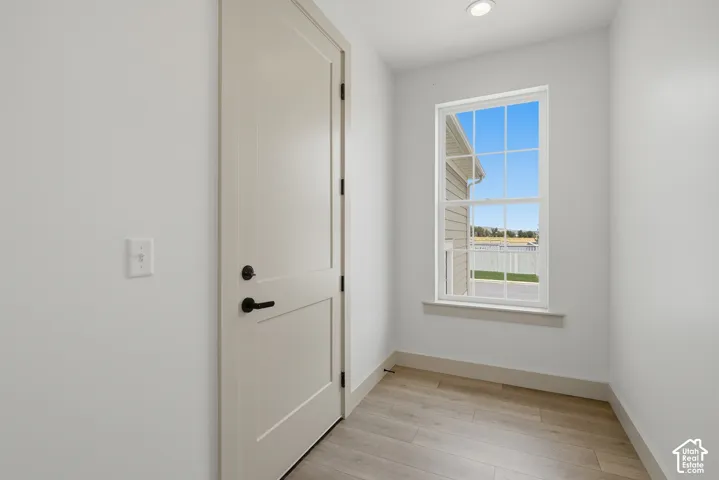 Light wood-finish flooring, a contemporary white door with matte black hardware, and a single-pane window with white trim