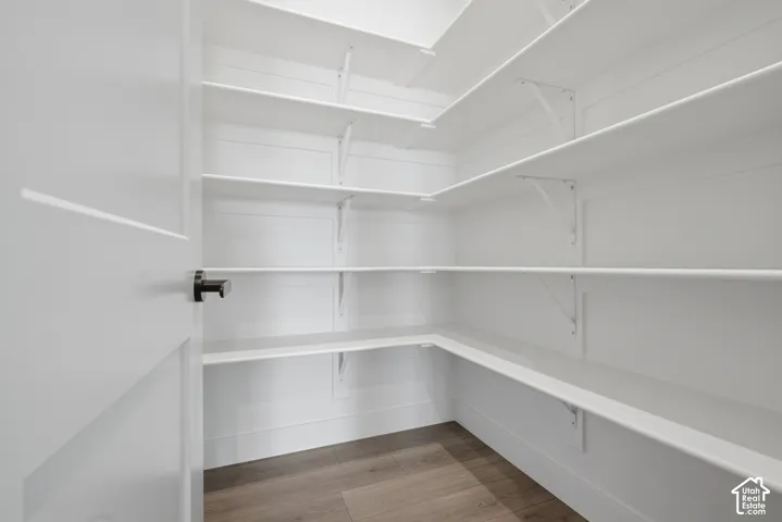 White paneled door with a black hardware, built-in shelving, white walls, and wood-finish flooring