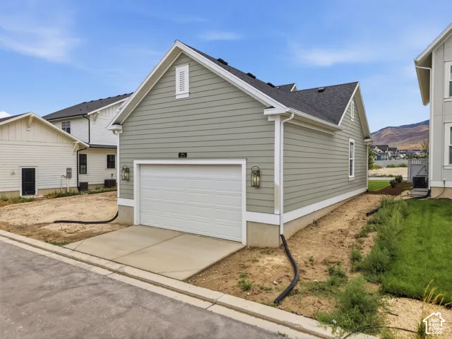 Light green horizontal siding with a white trim, featuring a white garage door, concrete driveway, and exterior lighting fixtures