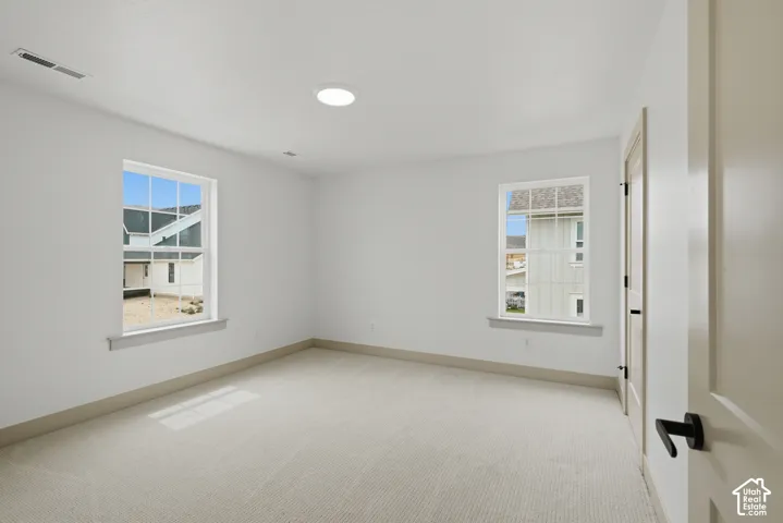 Recessed ceiling lighting, two double-hung windows, light-colored carpeting, and a solid interior door with black hardware