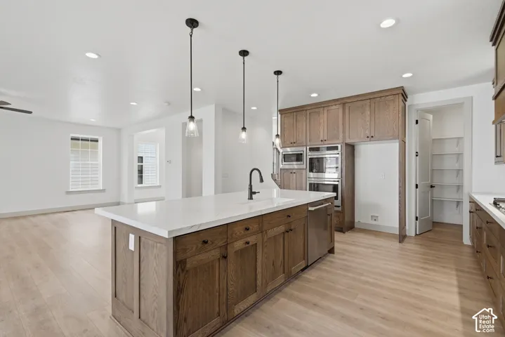 Kitchen island with a white countertop and integrated sink, pendant lighting, wood-finish flooring, double wall ovens, and a walk-in pantry