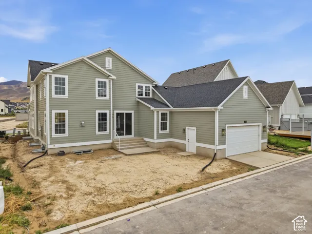 Newly constructed property featuring light green siding, white trim, a dark shingle roof, and an attached garage with a white door