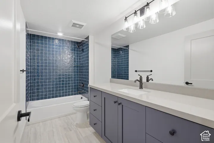 Bathroom featuring a white bathtub, blue tile shower surround, gray vanity with white countertop, and light wood-finish flooring