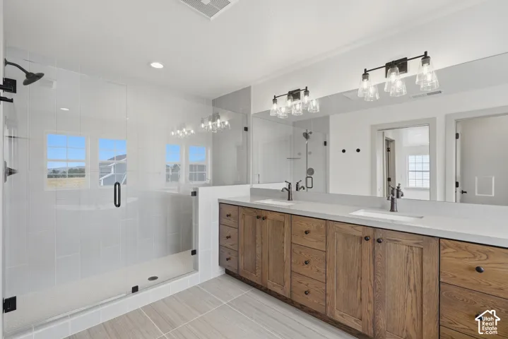 Primary Suite. Spacious bathroom featuring a frameless glass shower, dual vanity with wood-finish cabinetry, light-toned countertops, and rectangular under-mount sinks