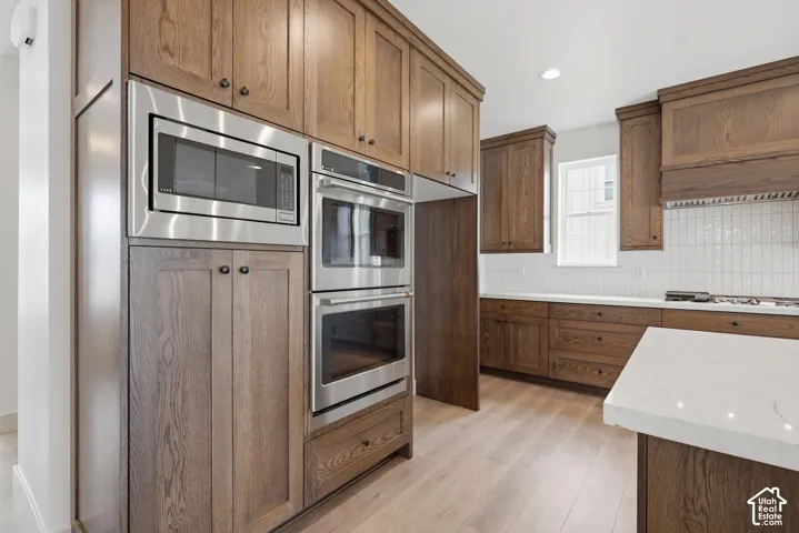 Wood-finish flooring, custom wood cabinetry, stainless steel microwave, double ovens, and white countertop surfaces