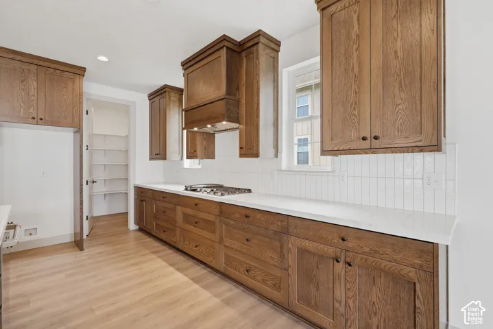 Wood-finish flooring, white countertops, white tile backsplash, wooden cabinetry, and a built-in pantry with shelving