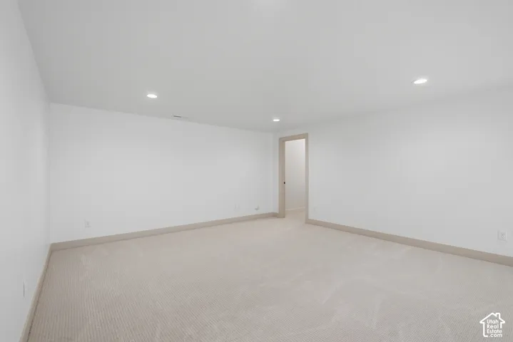 Spacious room featuring neutral carpeting, light-toned walls, recessed lighting, and a light wood-finish door frame