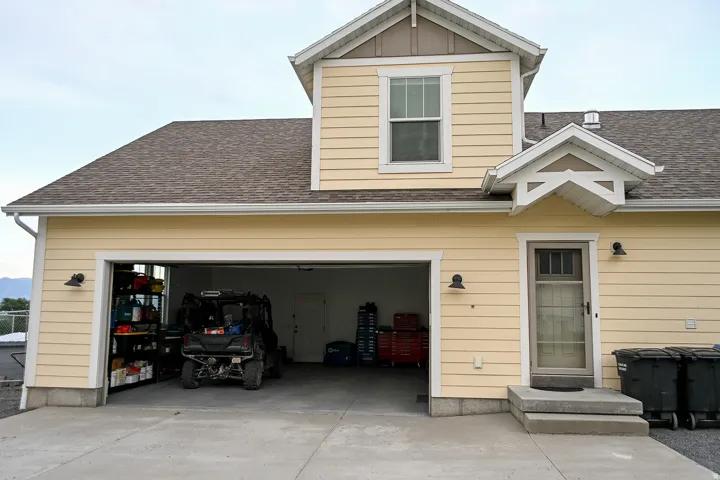 Two-car garage with concrete driveway, yellow siding exterior, second-story window dormer, and sheltered entry door