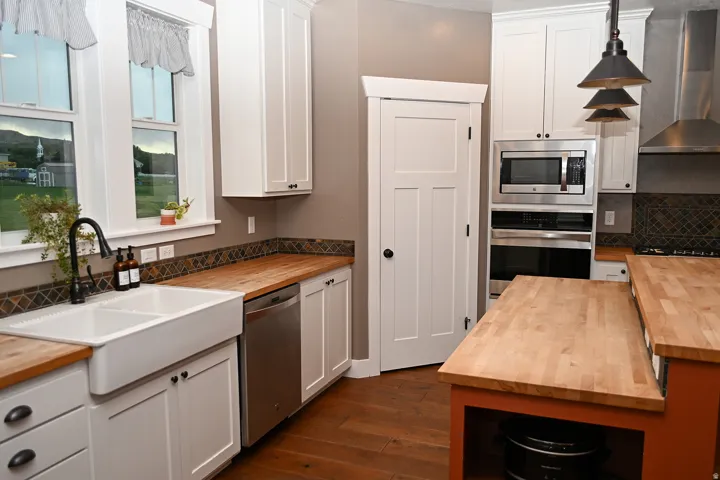 White shaker cabinetry, wood-finish countertops, stainless steel appliances, ceramic farmhouse sink, and a tiled backsplash