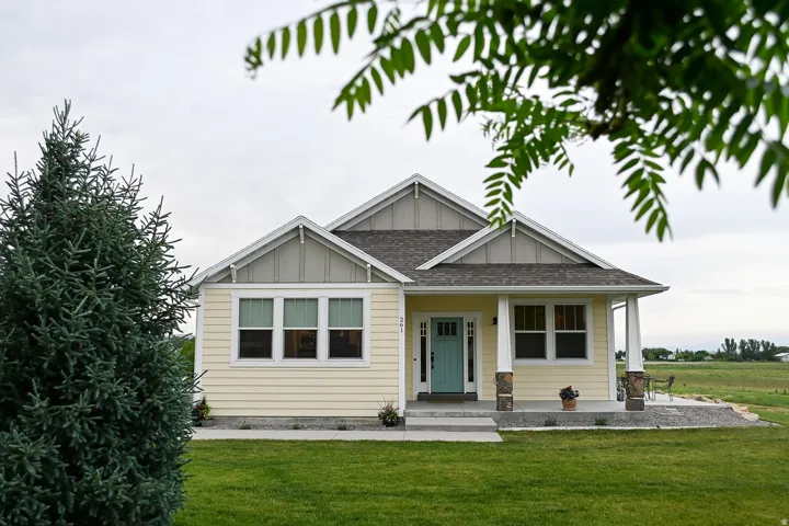 Yellow siding exterior with white trim, covered front porch, stone-accented columns, and a turquoise front door