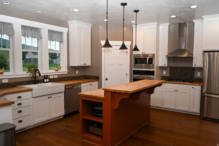 Chef's kitchen featuring white cabinetry with oil-rubbed bronze hardware, wood-finish countertops, stainless steel appliances including double wall ovens, a professional-range hood, and a substantial wood-finish island with open shelving