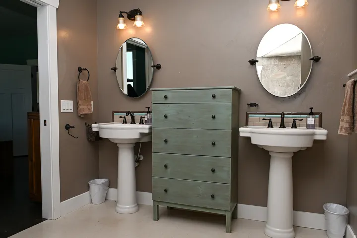 Dual pedestal sinks with dark bronze fixtures, oval mirrors, and wall-mounted lighting