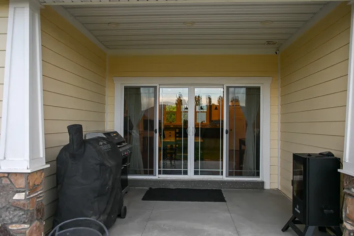 Covered patio with a concrete surface, white columns featuring a stone base, horizontal siding, and a sliding glass door
