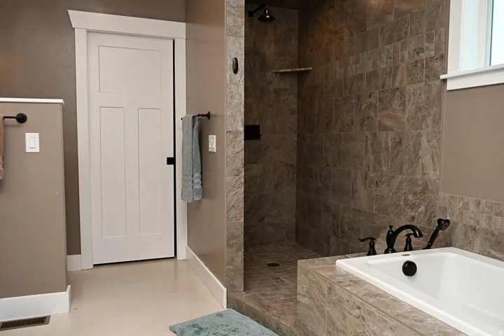 Built-in bathtub with black fixtures, tiled walk-in shower with a shelf, and a three-panel interior door