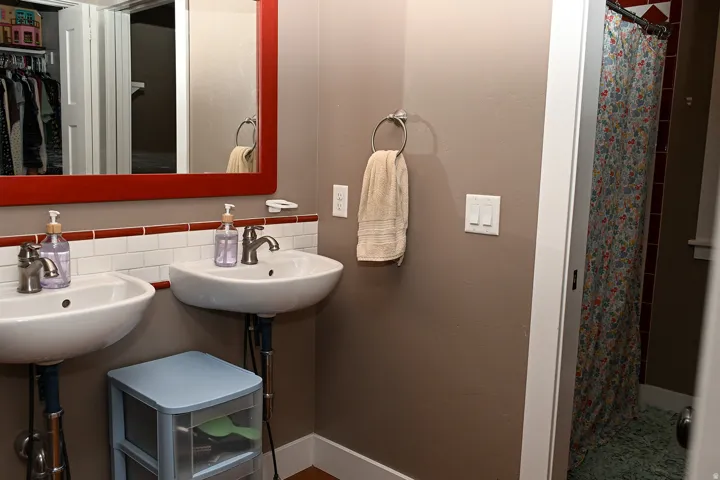 Dual wall-mounted sinks with contemporary faucets, white subway tile with a red accent, and a full-width framed mirror