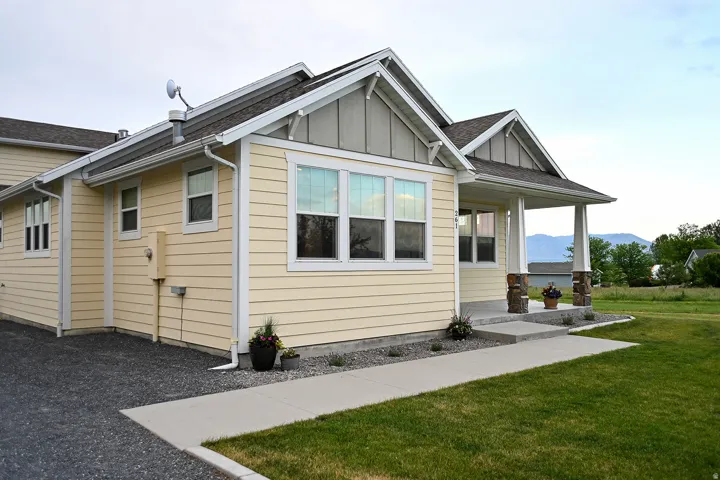 Property exterior featuring light yellow horizontal siding, a covered porch with stone-wrapped columns, and a concrete pathway leading to the entrance