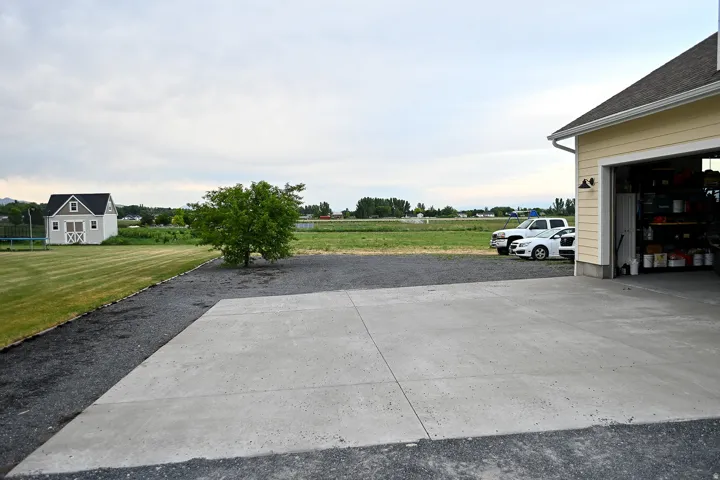 Concrete driveway with gravel borders, detached shed, and a mature tree