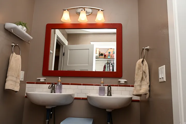 Dual white vessel sinks with chrome fixtures, complemented by white subway tile backsplash with brown trim