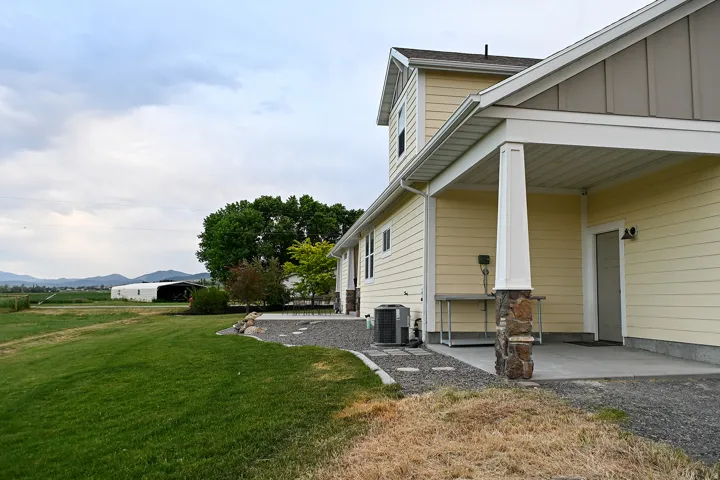 Yellow siding exterior with white trim, stone column accent, covered patio, and expansive green lawn