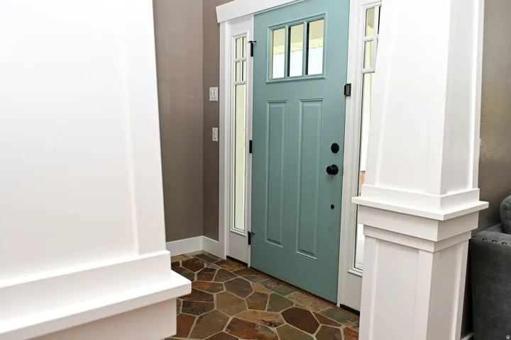Entryway featuring a patterned stone floor, a light blue front door with upper lites, surrounding sidelite windows, and white architectural columns