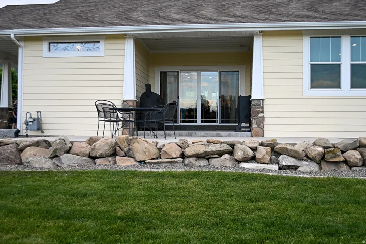 Covered patio with a concrete surface, stone accents on columns, and a rock retaining wall