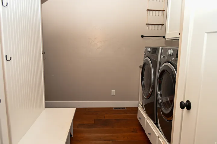 Wood-finish flooring with white baseboards, dedicated laundry appliances, and built-in cabinetry with black hardware