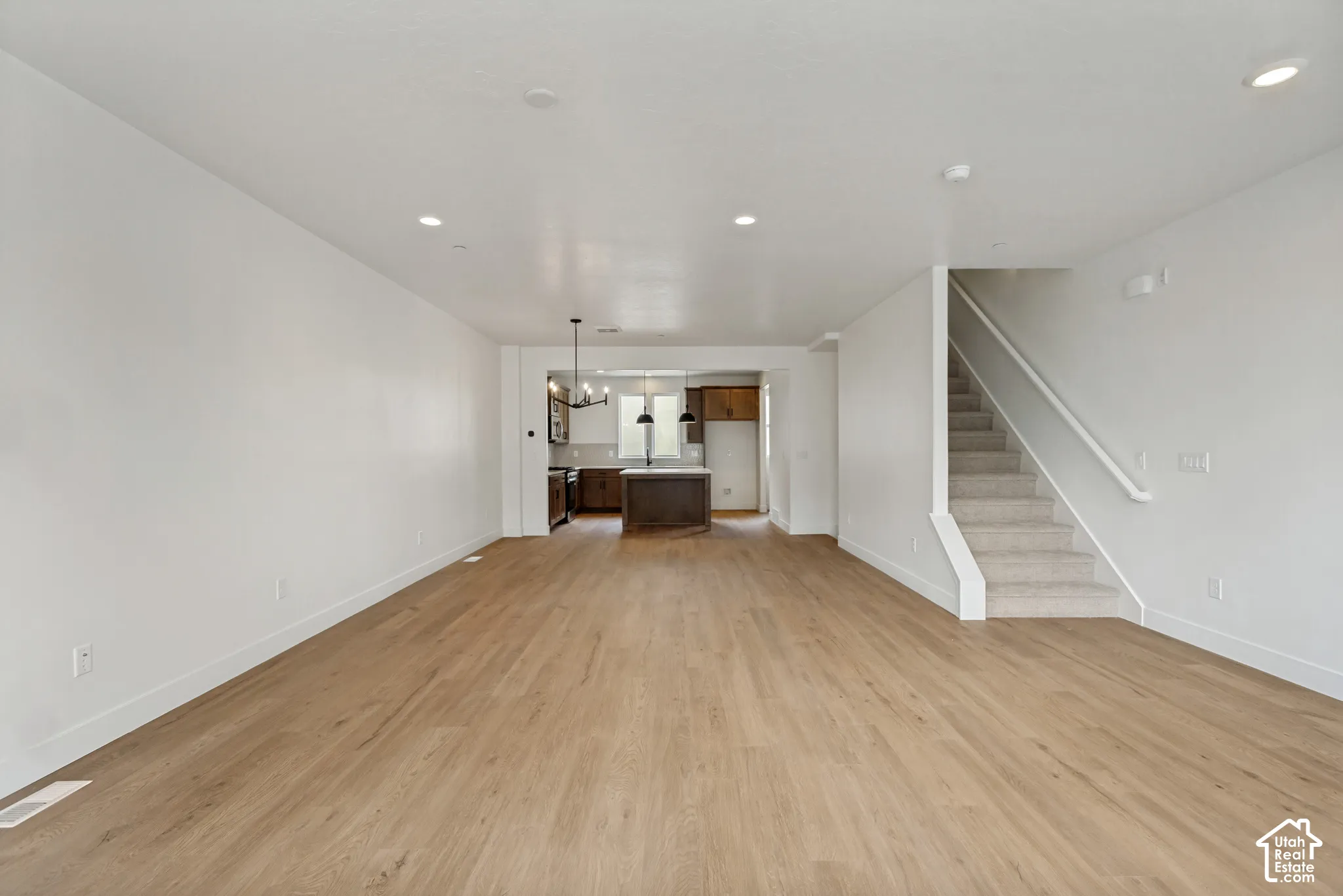 Open-concept living space featuring wood-finish flooring, recessed lighting, and a staircase with carpeted treads
