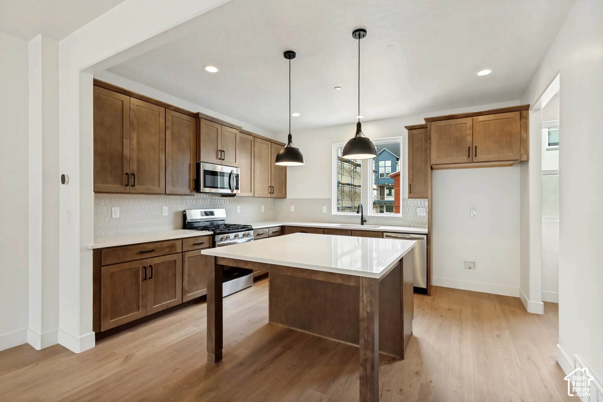 Kitchen featuring wood-finish cabinetry, stainless steel appliances, a center island with a light-toned countertop, recessed lighting, and pendant fixtures