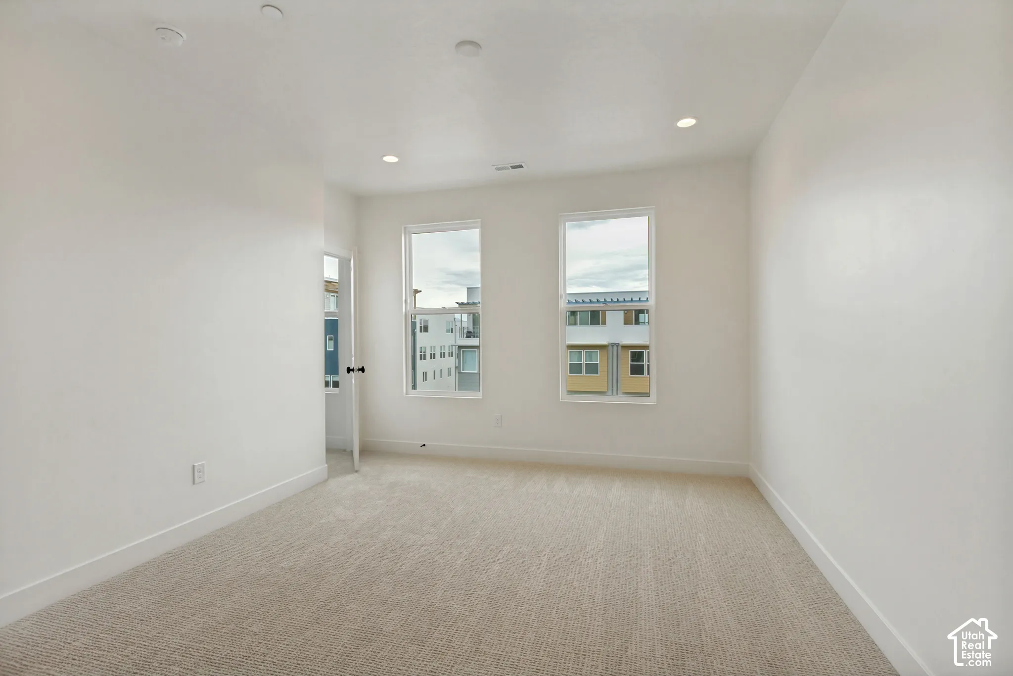Neutral-toned carpeting, recessed ceiling lighting, two windows, white walls, and white trim
