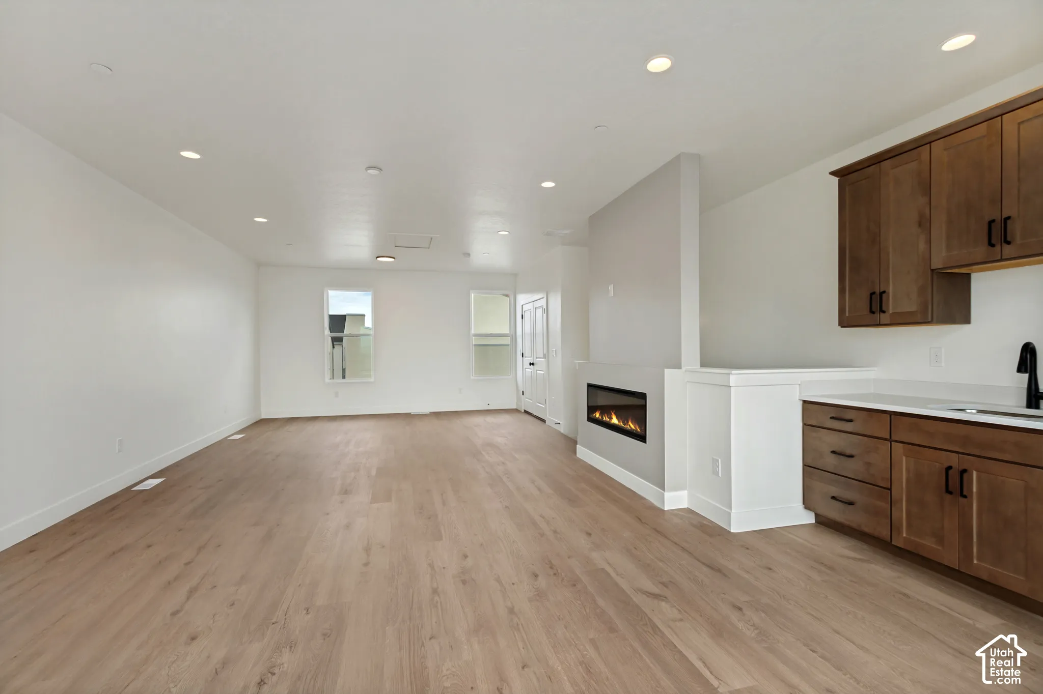 Open-concept living space featuring wood-finish flooring, recessed lighting, a linear fireplace, and built-in cabinetry with a countertop and sink