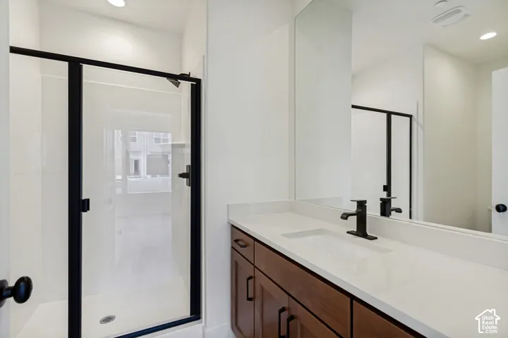 Walk-in shower with black-framed glass enclosure, single vanity with wood cabinetry, light-toned countertop, and undermount sink, complemented by a matte black faucet