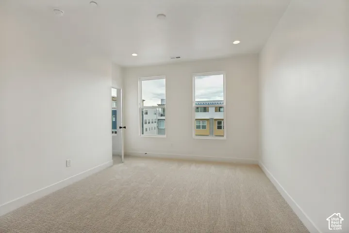 Neutral-toned carpeting, recessed ceiling lighting, two windows, white walls, and white trim