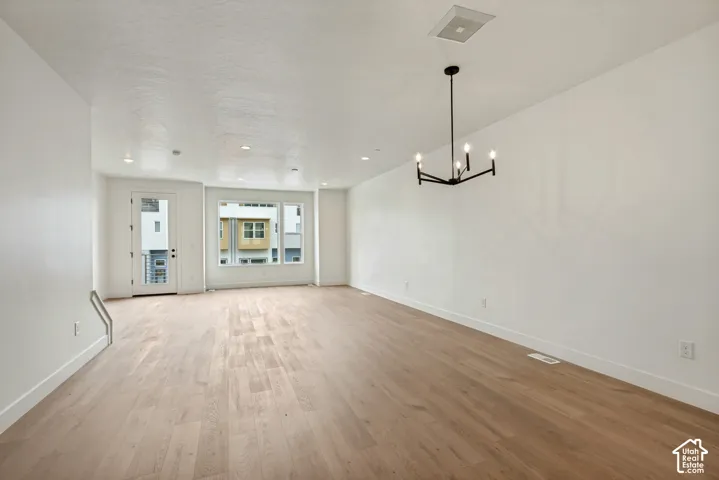 Spacious room featuring wood-finish flooring, white walls, recessed lighting, and a modern black chandelier