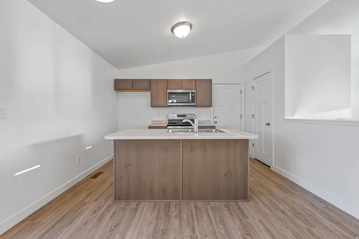 Central island with integrated sink, wood-finish flooring, wood-finish cabinetry, stainless steel microwave, and stainless steel range