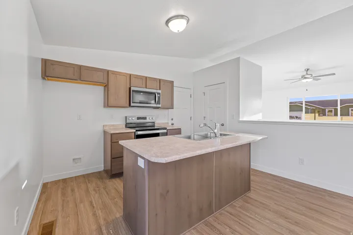 Kitchen with wood-finish flooring, island featuring an integrated sink, brown cabinetry, and stainless steel appliances