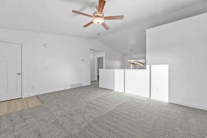 Vaulted ceiling with a ceiling fan, carpeted flooring, white paneled interior door, and a partial wall separation