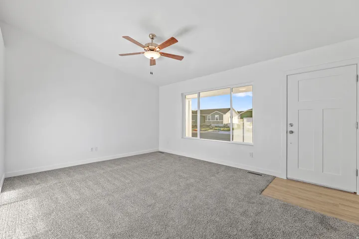 Spacious room featuring vaulted ceilings, a contemporary ceiling fan with integrated lighting, expansive windows, durable carpeting, and a panel-style entry door